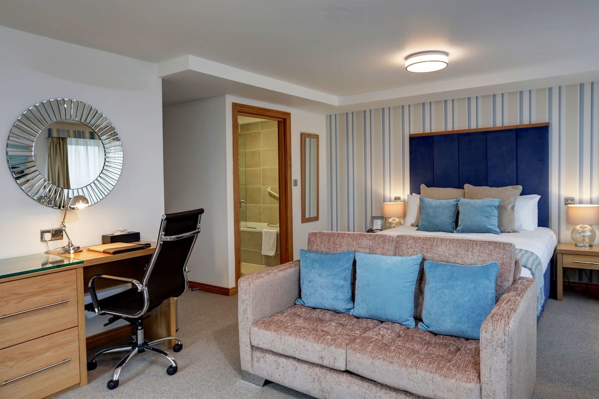 Une chambre d’hôtel avec un lit, un bureau, une chaise, un canapé, un miroir et une porte de salle de bain.
