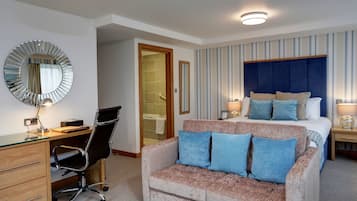 A hotel room with a bed, a desk, a chair, a sofa, a mirror, and a bathroom door.
