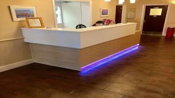 Un comptoir d’accueil avec un revêtement en bois et une bande lumineuse à LED bleue. Il y a des horloges au-dessus du comptoir et un tableau encadré au mur.