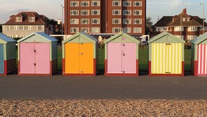 Una hilera de cabañas de playa coloridas con un edificio residencial grande al fondo.