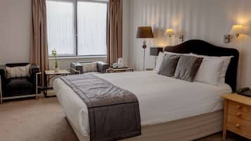 A hotel room with a large bed, bedside tables, a desk, a chair, and a window with curtains.