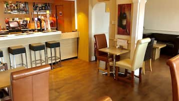 A bar area with stools, a counter with bottles, and a seating area with chairs and a table.