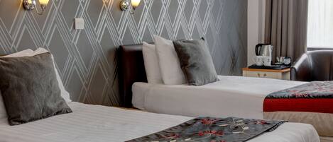 A hotel room with two beds, a nightstand, a chair, and a wall with patterned wallpaper.