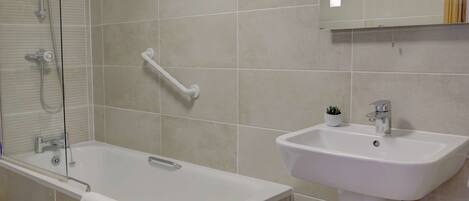 A bathroom with a bathtub, a sink, a handrail, and a mirror.