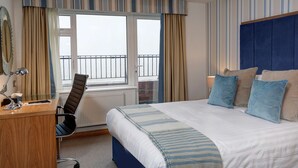 Habitación de hotel con cama, escritorio, silla, ventana con cortinas y vistas al balcón exterior.