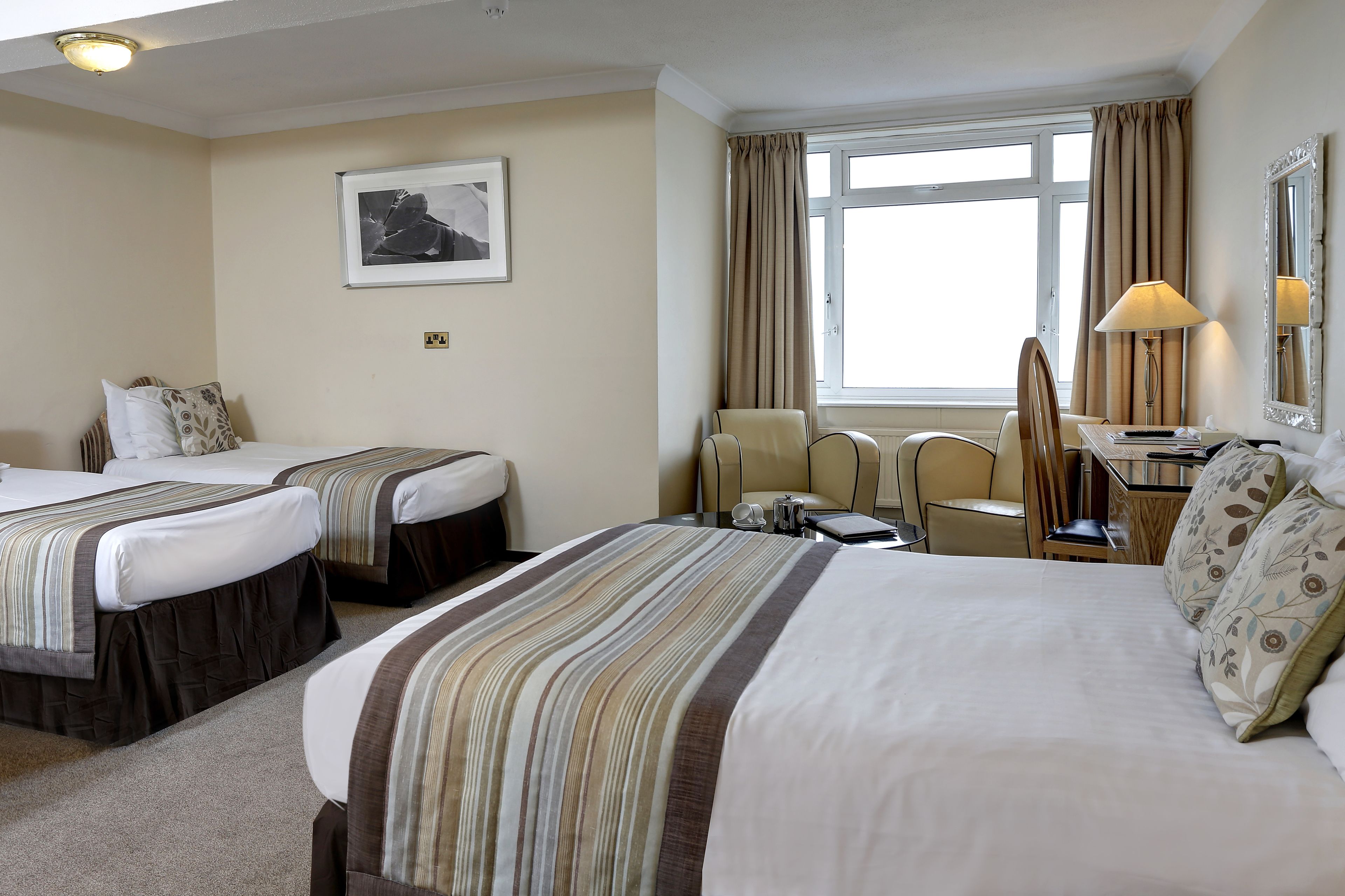 A hotel room with two beds, a desk, a chair, a lamp, and a window with curtains.