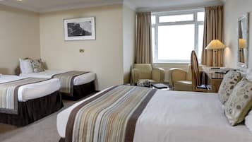 Habitación de hotel con dos camas, un escritorio, una silla, una lámpara y un ventanal con cortinas.