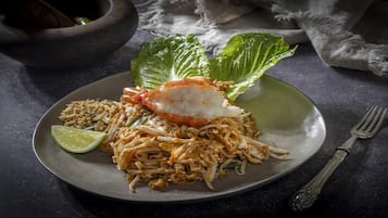 A plate of Pad Thai with shrimp, lime, and bean sprouts on a dark plate.