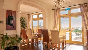 Un área de comedor con vista a la ciudad, que incluye una araña, plantas en macetas y un cuadro con botellas de vino.