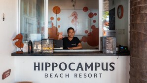 Een receptiebalie bij Hippocampus Beach Resort, met een houten bord erboven en een muur met een rond patroon.