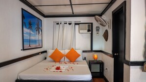 Een hotelkamer met een bed, een nachtkastje met een lamp, een schilderij van een strand en een airconditioning.