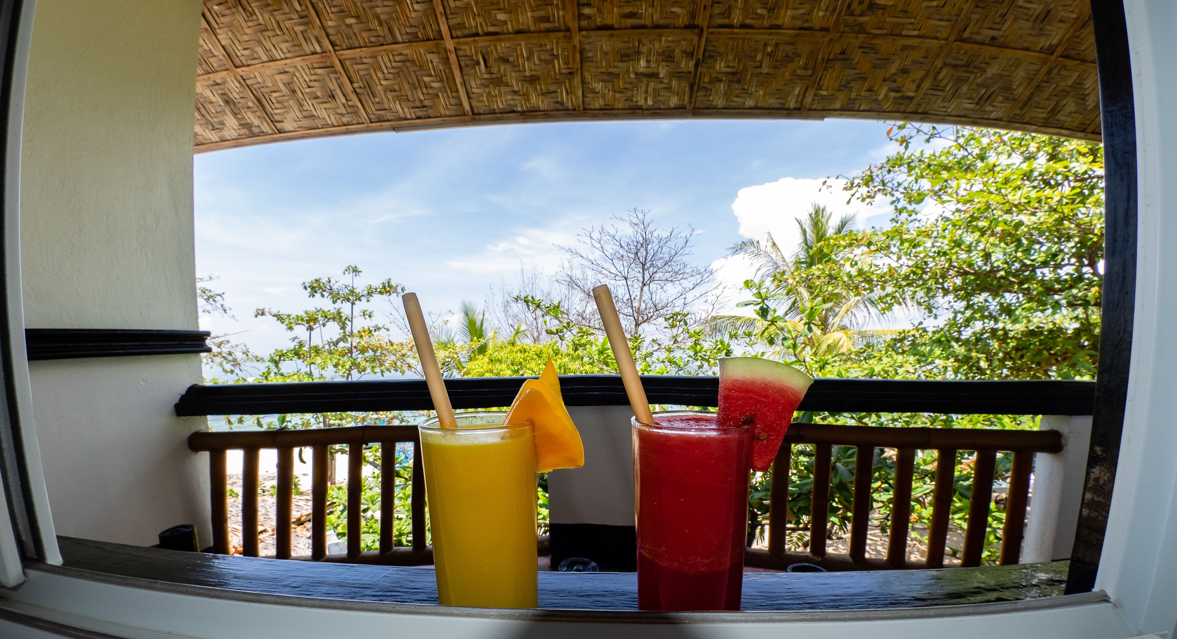 A balcony with two drinks, one yellow and one red, with a view of trees and sky.