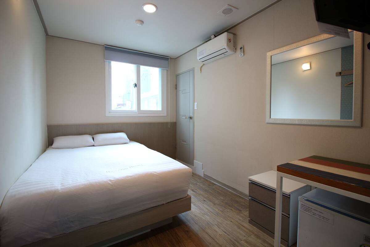 Un dormitorio con cama, escritorio, espejo y aire acondicionado.