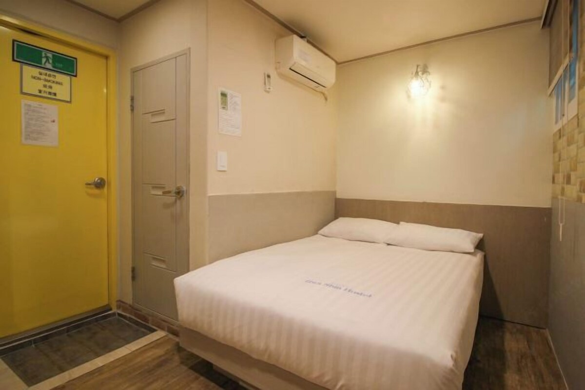 A hotel room with a bed, a door, and an air conditioning unit.