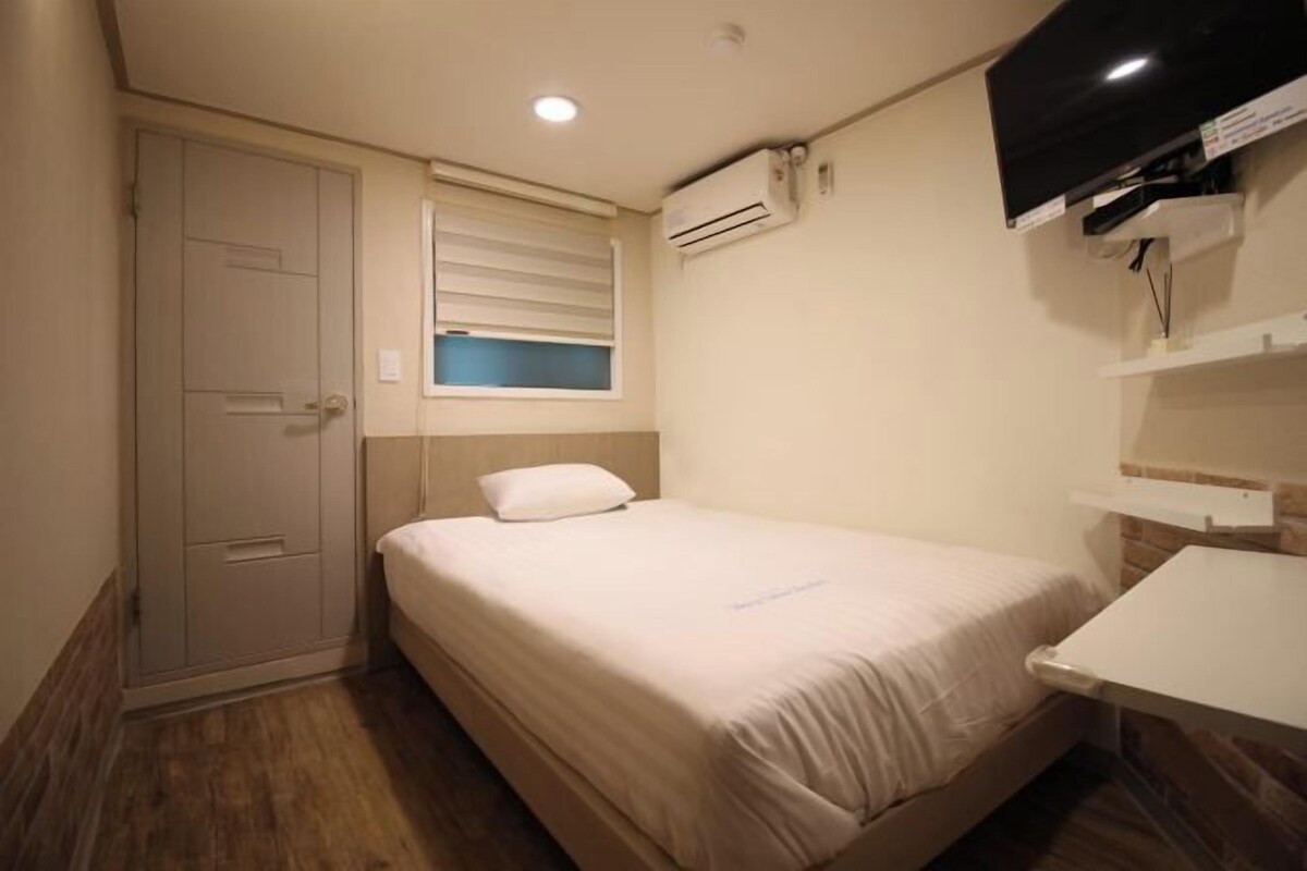 A small, neatly arranged bedroom with a single bed, a bedside table, a wardrobe, and a mounted TV.