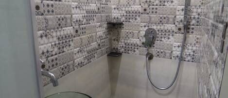 A bathroom with patterned tiles, a glass basin, and a shower with a handheld showerhead.