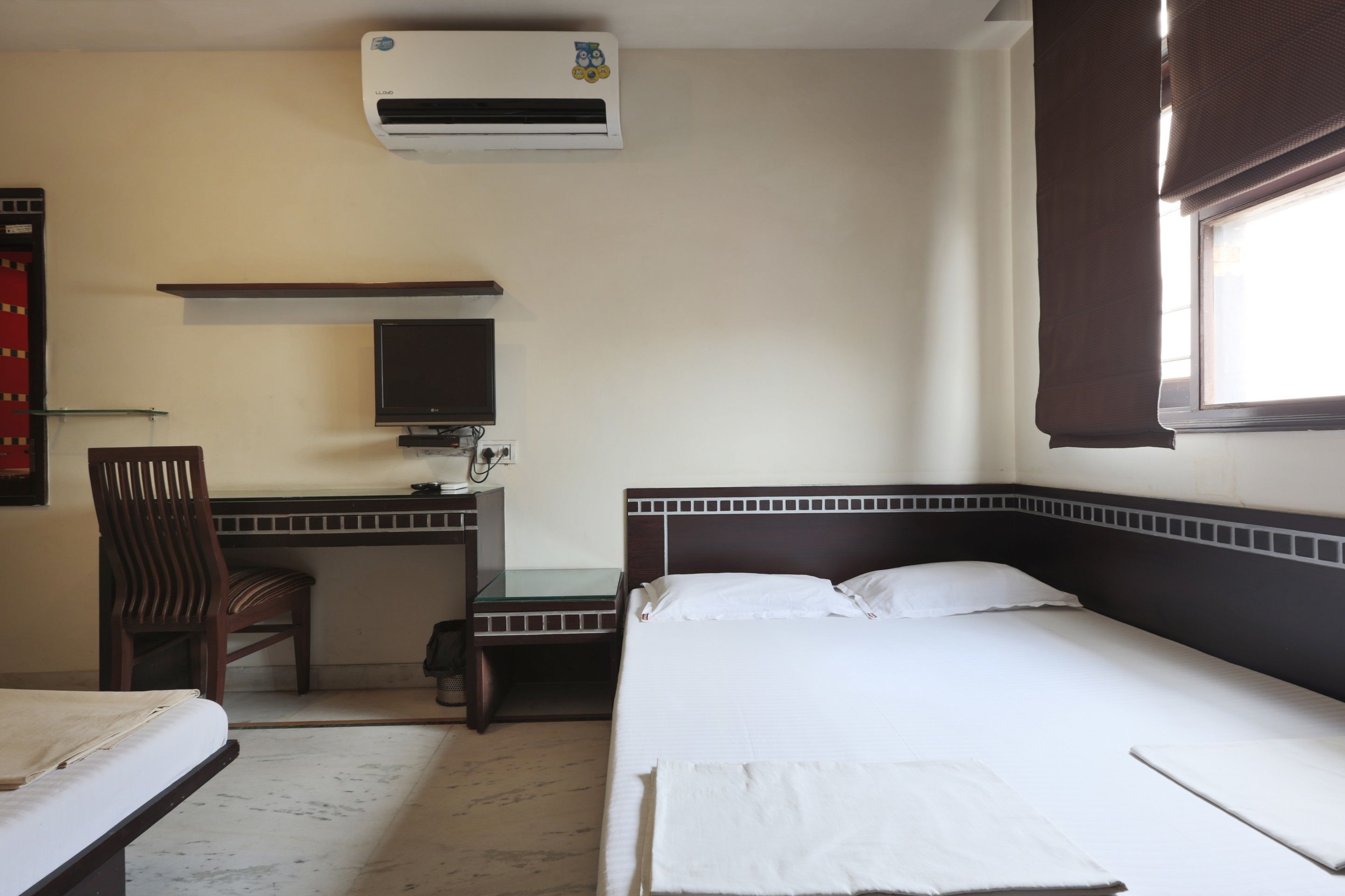 A hotel room with a bed, a desk with a chair, a television, and an air conditioning unit.