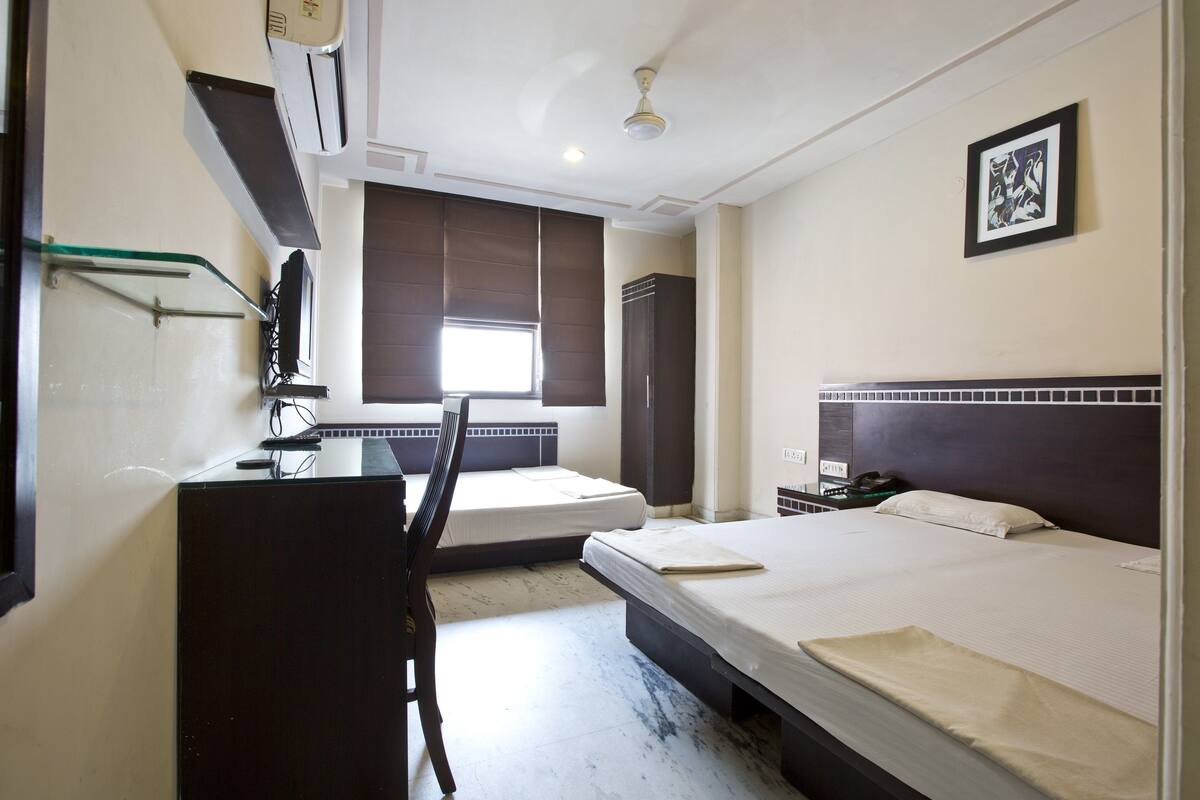 A hotel room with a bed, a desk, a chair, a wardrobe, and a window.