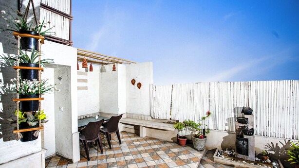 Un patio con suelo de baldosas, una zona de estar con sillas, plantas en macetas y una pequeña fuente.