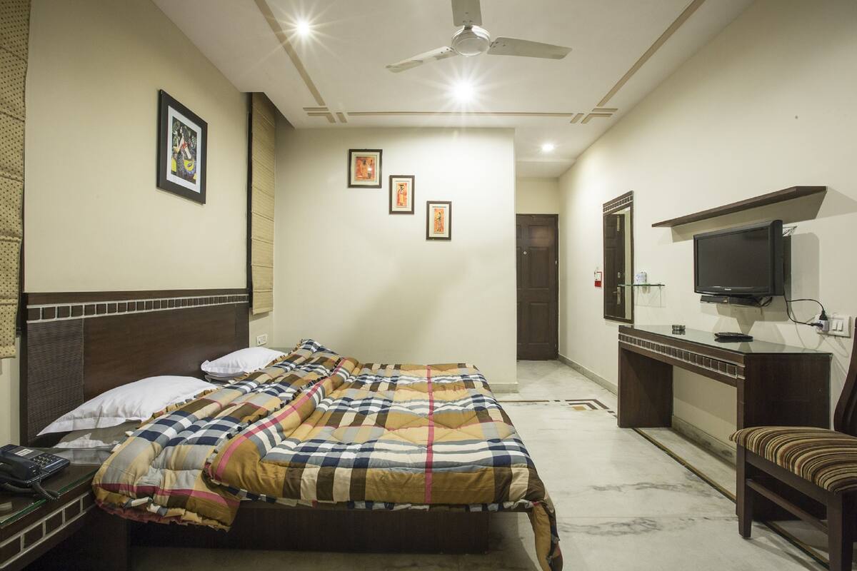 A hotel room with a bed, bedside table, TV, and a desk with a chair.