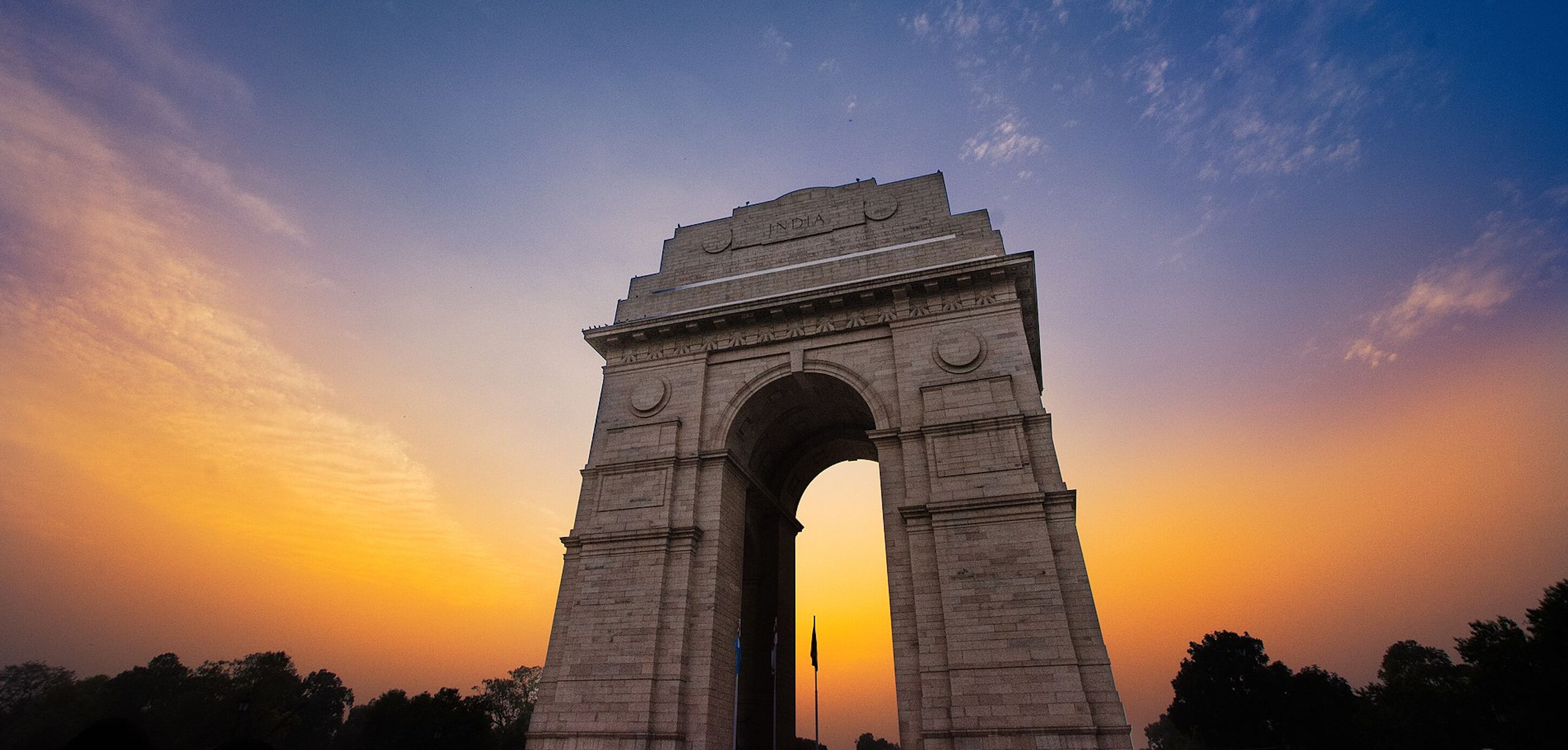 Een groot stenen monumentaal bogen met inscripties, gelegen voor een zonsondergang.