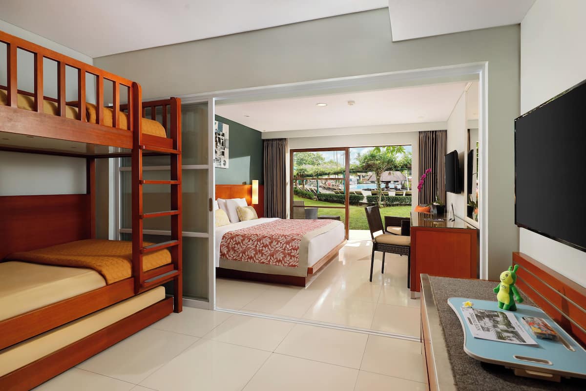 Een hotelkamer met een stapelbed, een enkel bed, een bureau, een televisie en uitzicht op de tuin.