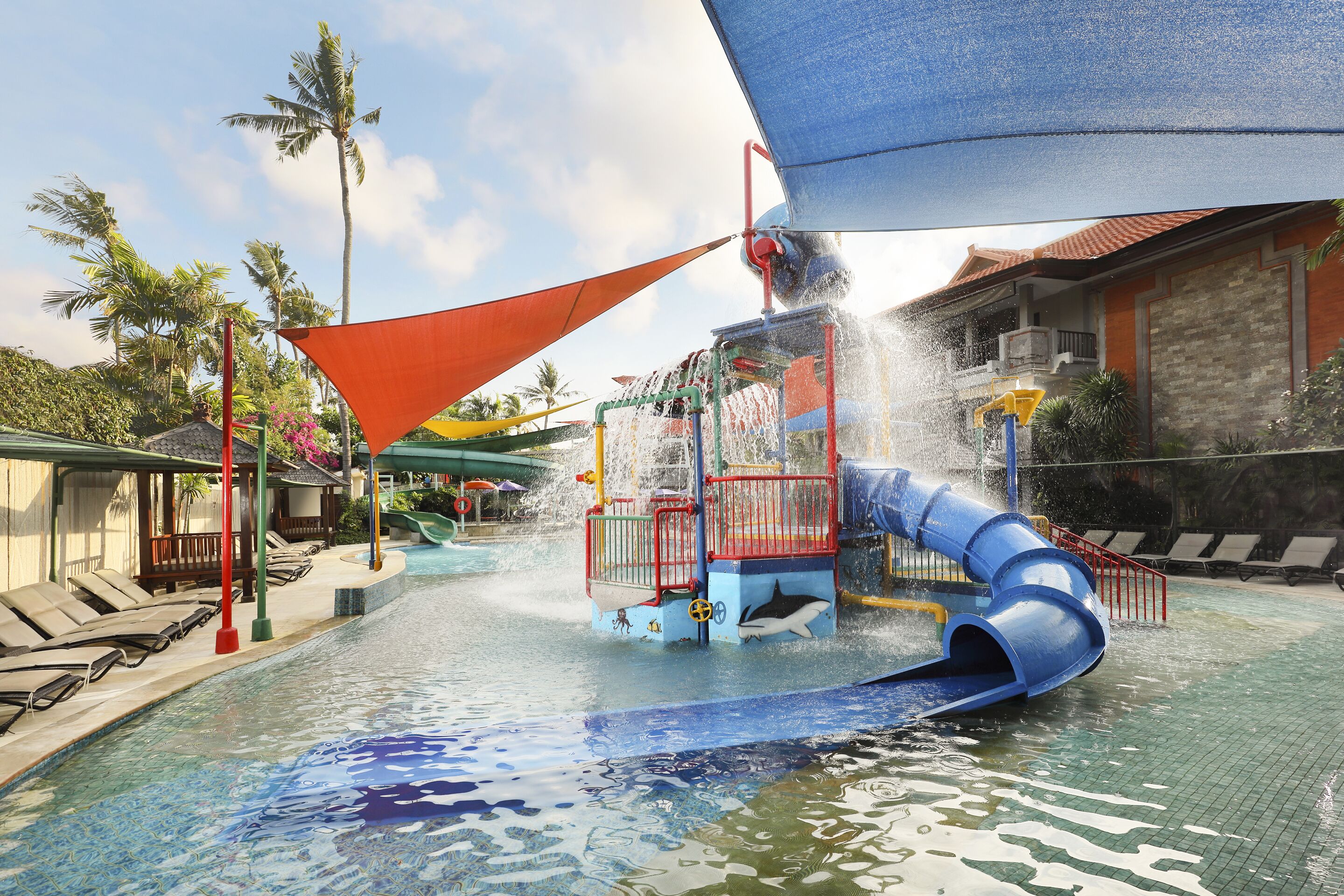 Un parque acuático con un tobogán de agua azul, una piscina y una zona cubierta con sillones de descanso.