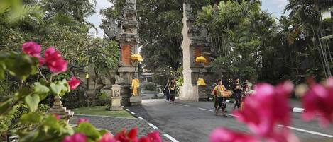 A temple entrance with traditional architecture, a paved pathway, and lush greenery.