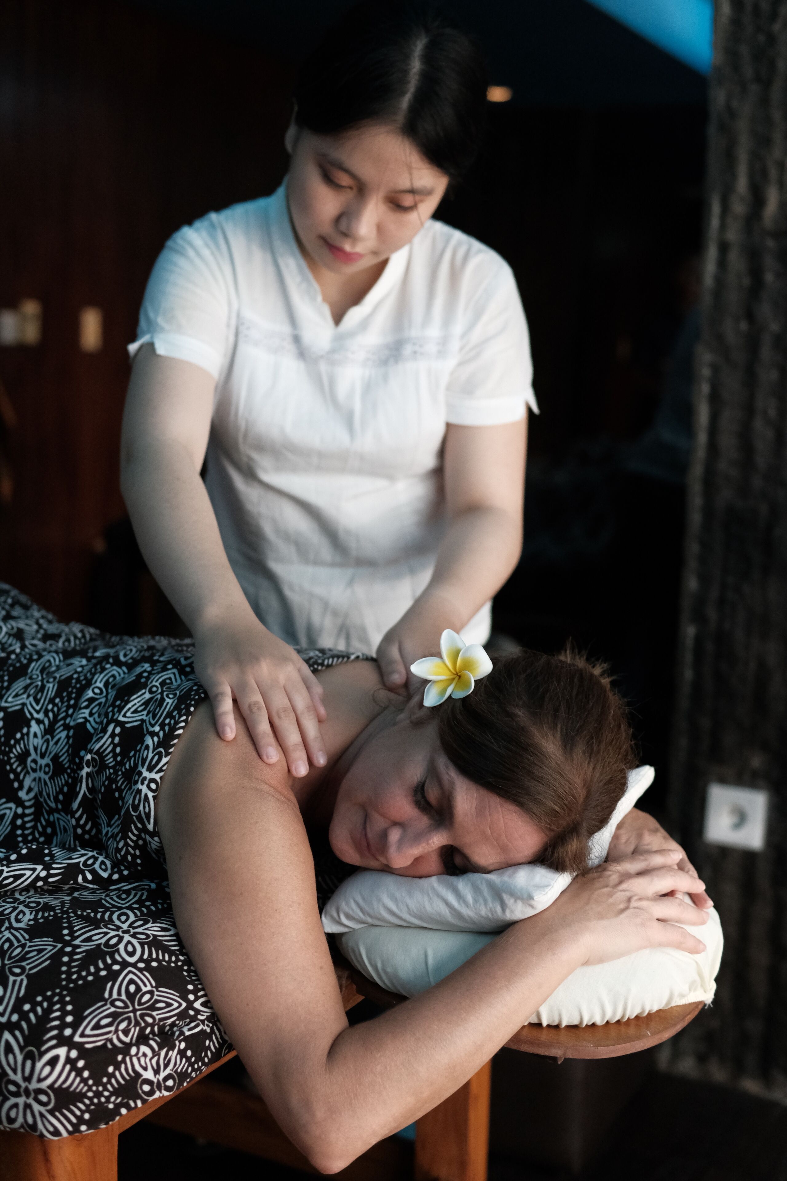 En massageterapeutisk session i et rum med et mønstret sengetæppe og en træsenggavl.
