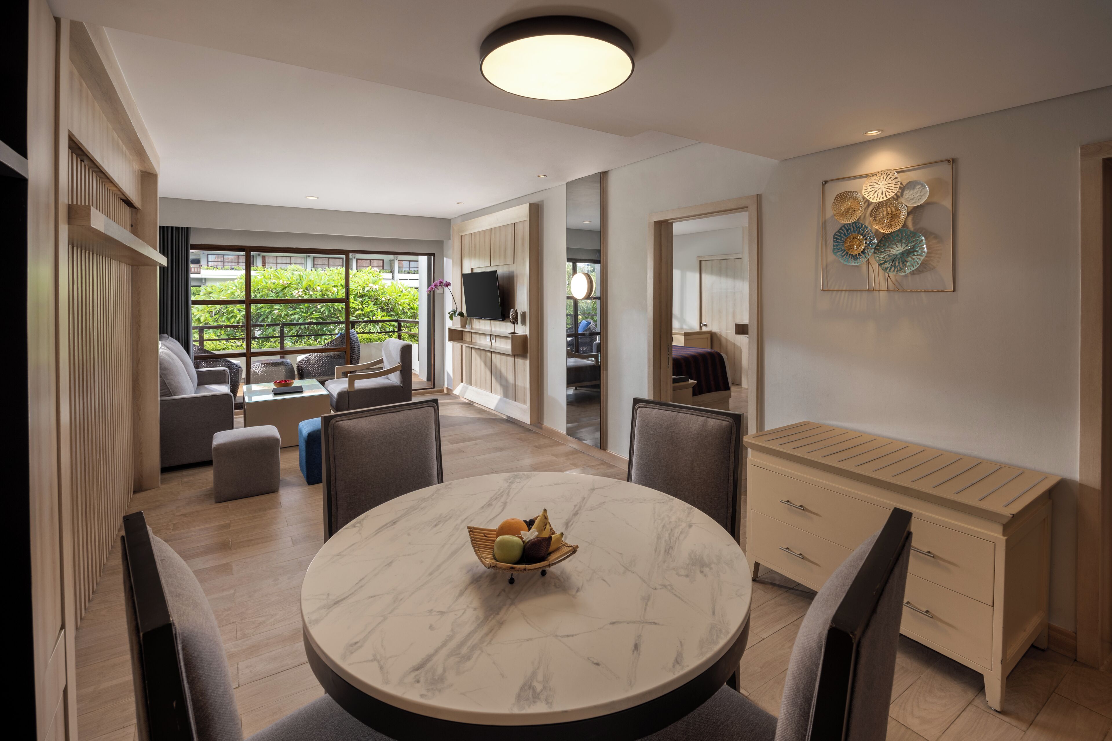 A modern living room with a round marble table, grey sofas, a TV, and a large window.