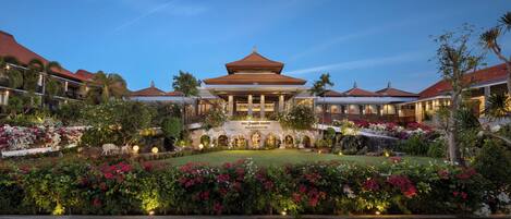 A traditional building with a central pavilion, surrounded by lush gardens and palm trees.