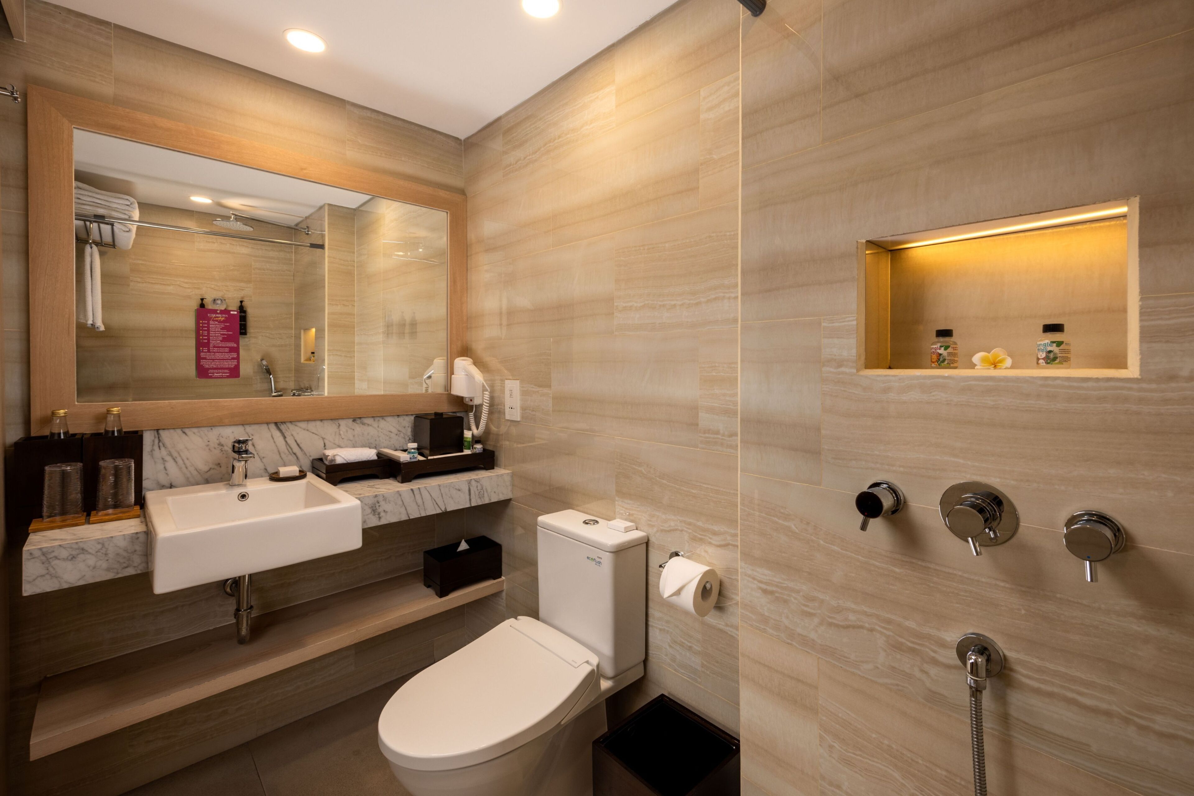Een moderne badkamer met een marmeren wastafel, toilet, douche met een handdouche en een spiegel met handdoekhouder.