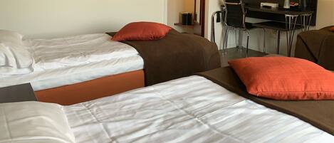 A hotel room with two beds, each with white linens and red pillows. There is a small desk with a chair and a trash can.