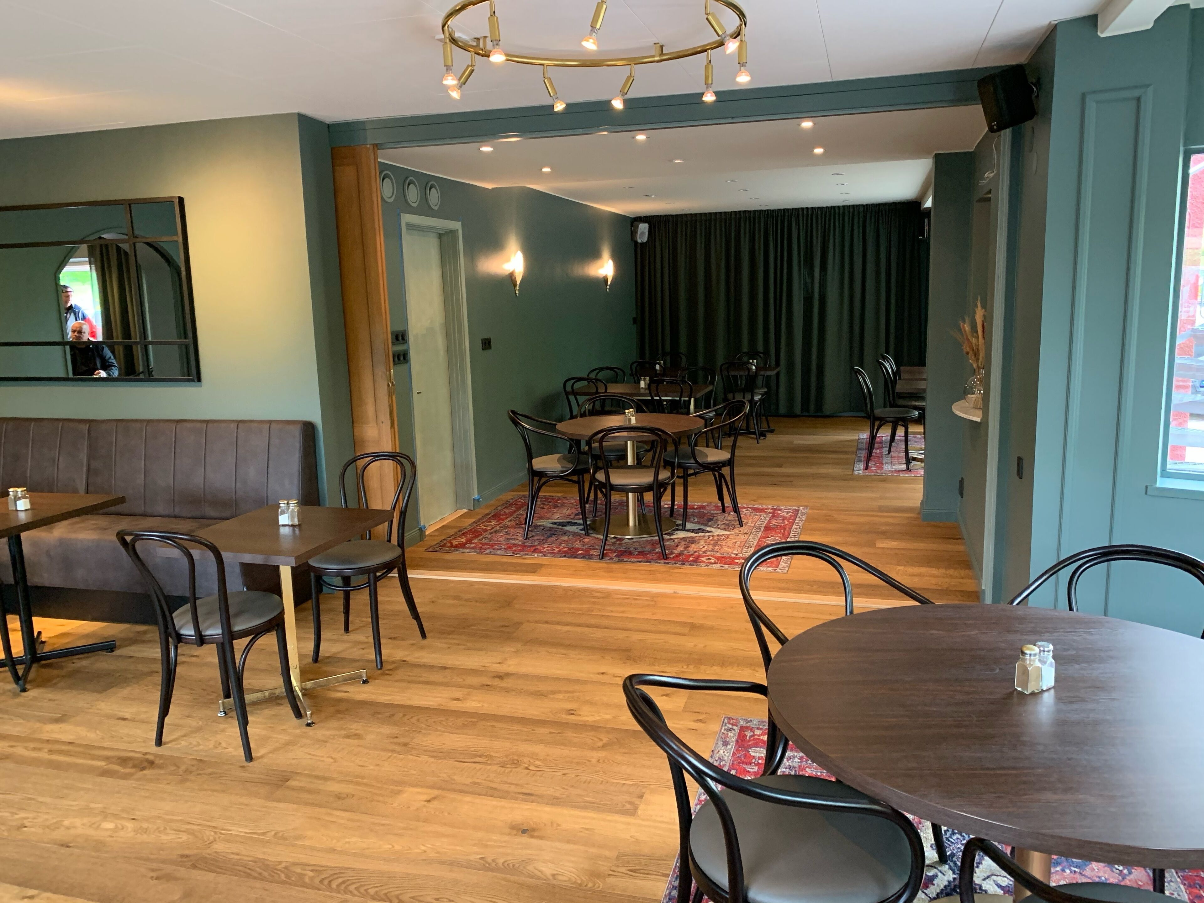 Een restaurantinterieur met houten vloeren, ronde tafels en donkere stoelen. Er staan meerdere eettafels in het midden, omringd door zitjes aan de zijkanten.