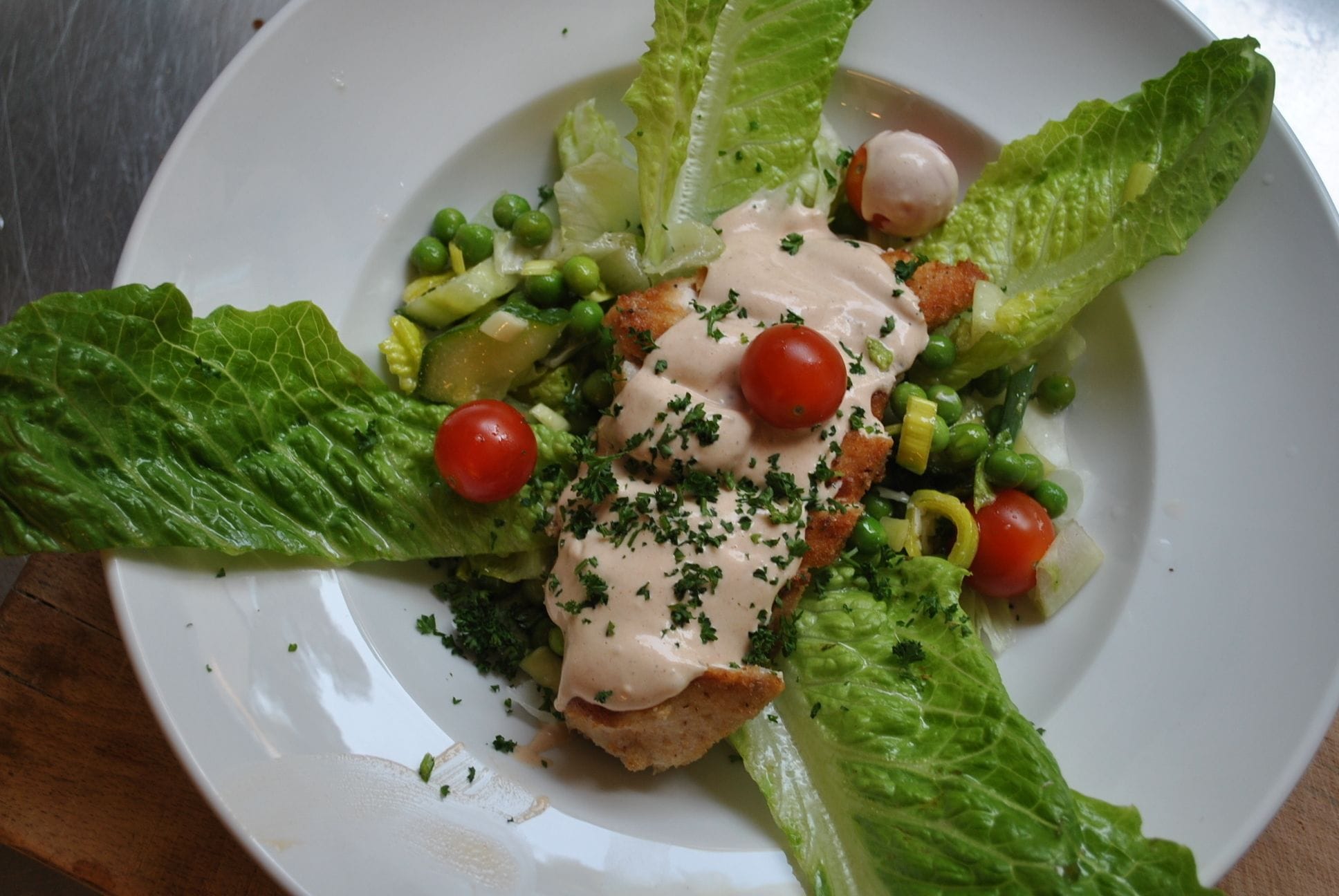 En tallrik med mat bestående av sallad, ärtor, körsbärstomater och en krämig sås.