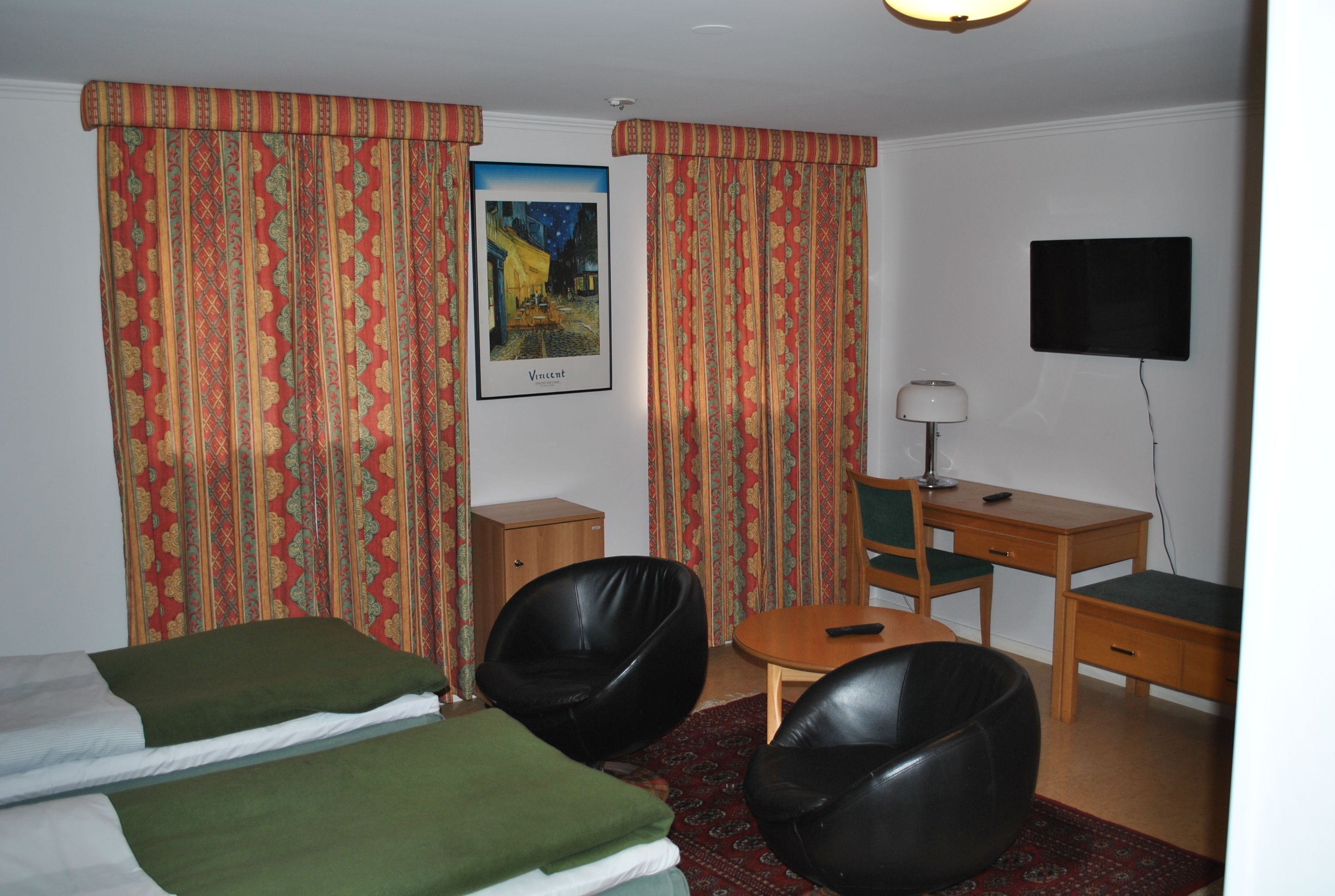 Ein Hotelzimmer mit zwei Betten, einem Schreibtisch, einem Stuhl, einem Fernseher und einem Gemälde an der Wand.