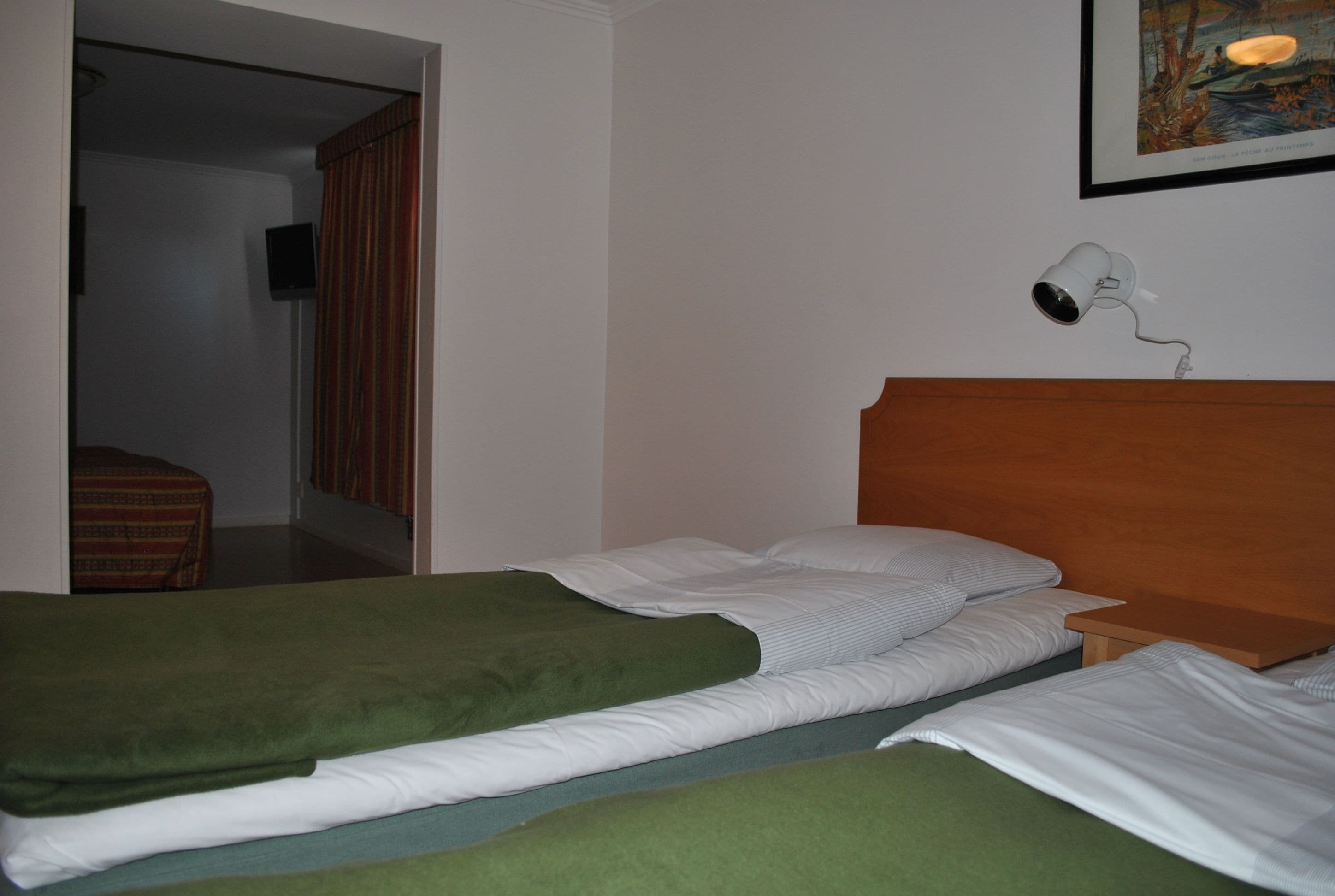 A room with two beds, a wooden headboard, a wall-mounted light, and a framed picture.