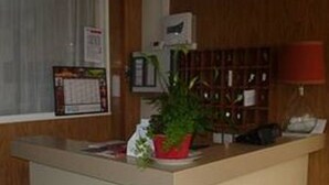 A reception area with a counter, a potted plant, a clock, and a window with blinds. - Hotel Des Vosges (Paris)