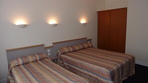 A room with two single beds, each with a patterned bedspread, a wooden headboard, and a wall-mounted light fixture. - Hotel Des Vosges (Paris)