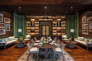 A spacious dining area with a long wooden table, surrounded by upholstered sofas and chairs, with a decorative wall in the background.