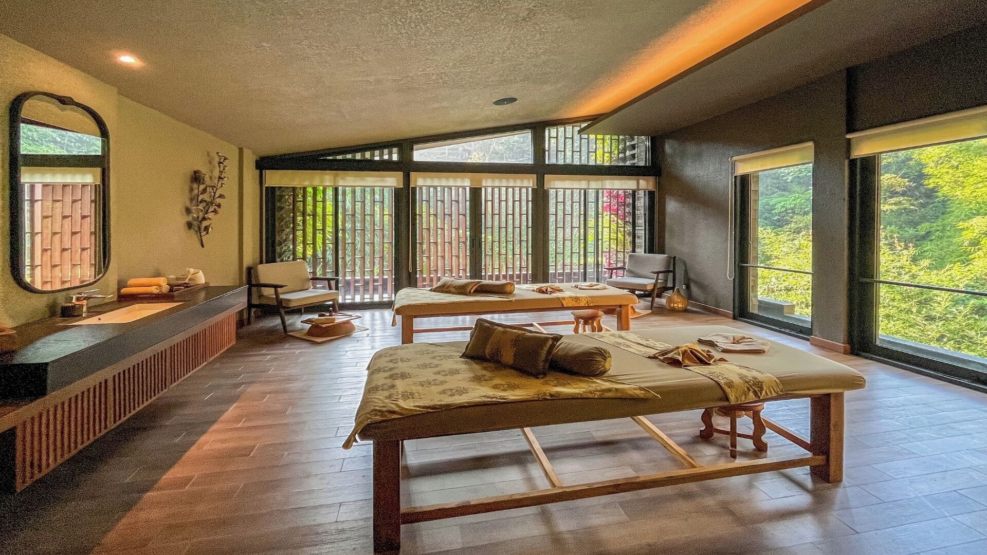 A room with two beds, a sitting area, and large windows.