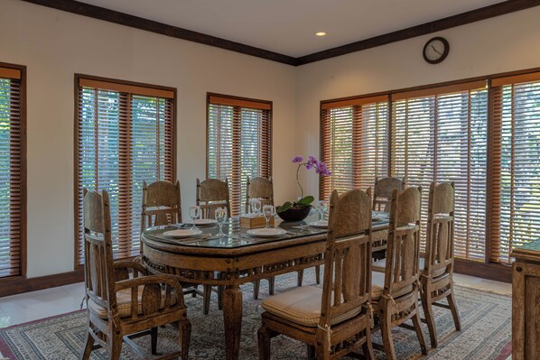 Uma sala de jantar com uma mesa redonda, cadeiras de madeira e um relógio na parede.