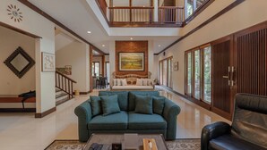 A spacious living area with a green sofa, a black leather chair, and a coffee table. A staircase leads to an upper level. - Plataran Puncak Residences (Cisarua)
