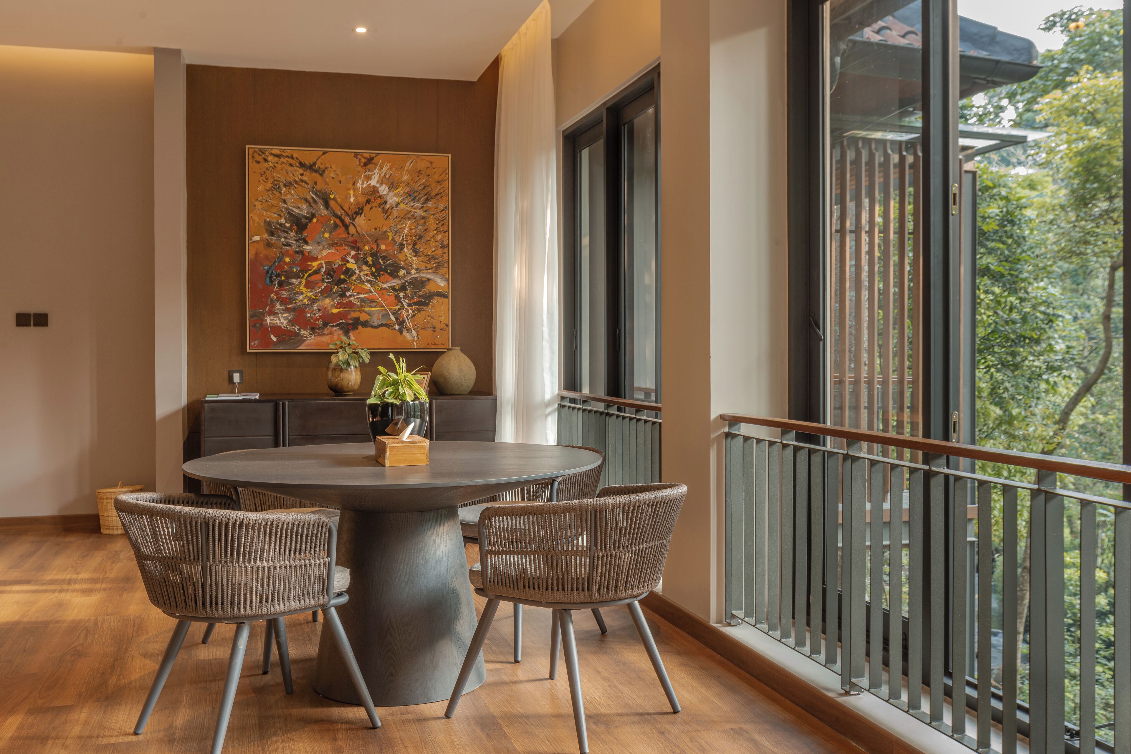 A modern dining area with a round table, wicker chairs, and a large abstract painting on the wall.