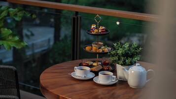 A round wooden table with a tiered dessert stand, two cups of tea, a teapot, and a small potted plant.