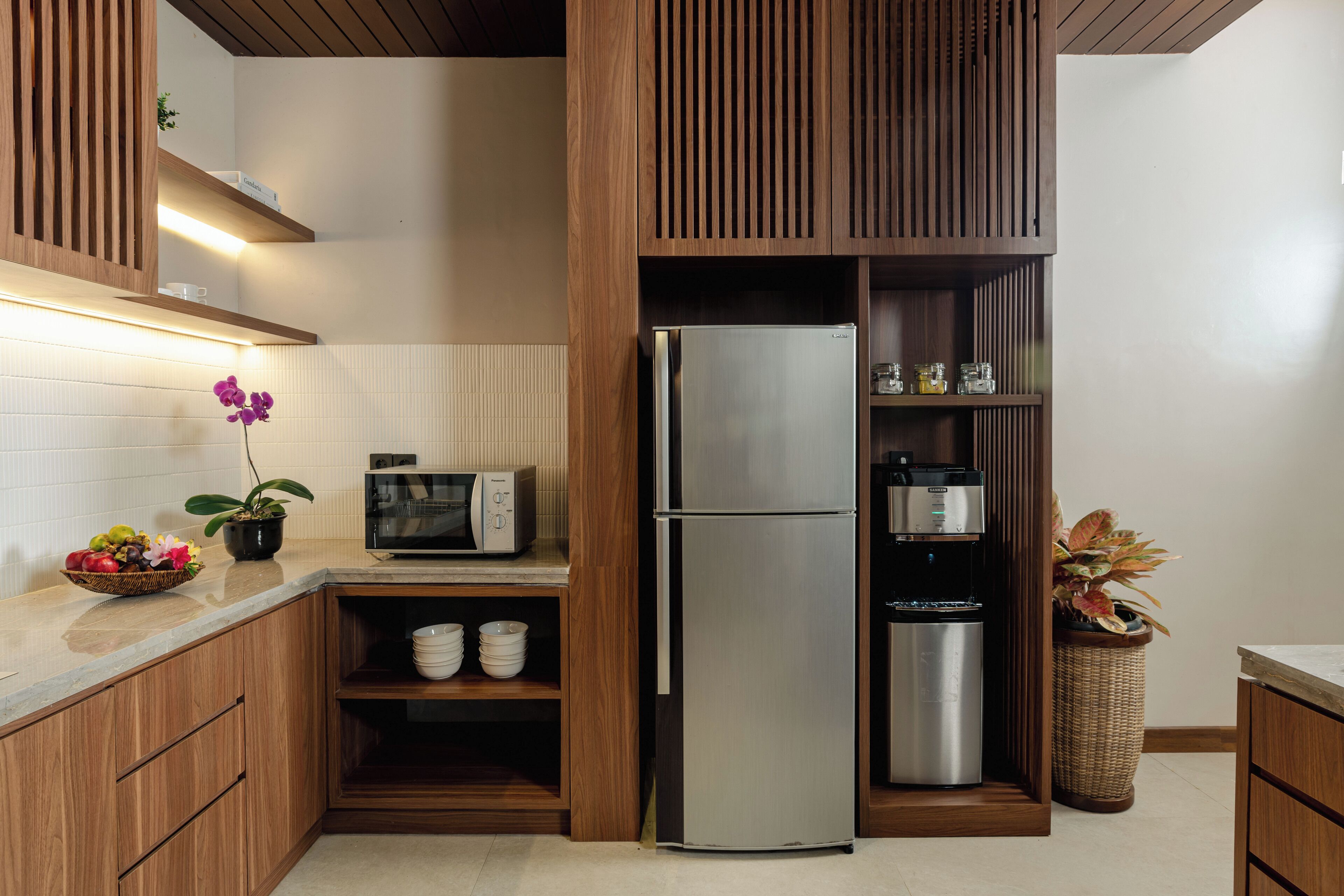 A modern kitchen with wooden cabinets, a stainless steel refrigerator, a microwave, and a coffee machine.
