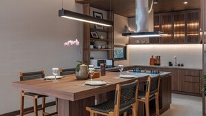A modern kitchen with a central island, wooden cabinetry, and built-in appliances. - Plataran Puncak Residences (Cisarua)