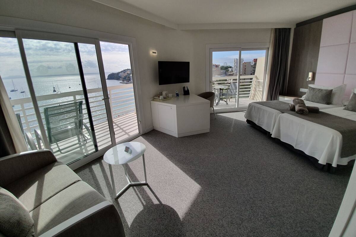 Ein Hotelzimmer mit Bett, Schreibtisch, Fernseher und einem Balkon mit Meerblick.