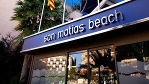 A hotel named 'Hotel Son Matias Beach' with a modern glass facade, palm trees, and flags including the EU flag. - Hotel Son Matias Beach - Adults Only (Calvia)