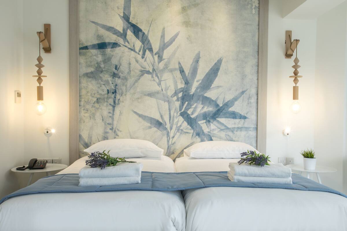 A modern hotel room with a large bed, two bedside tables, a wall-mounted phone, and a wall art piece.